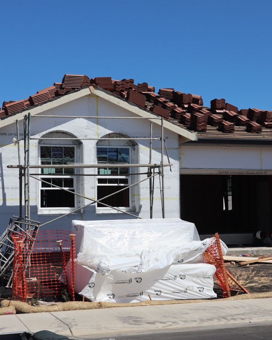 Moradia térrea em construção, paredes brancas, andaimes e telhas de barro empilhadas na cumeeira.