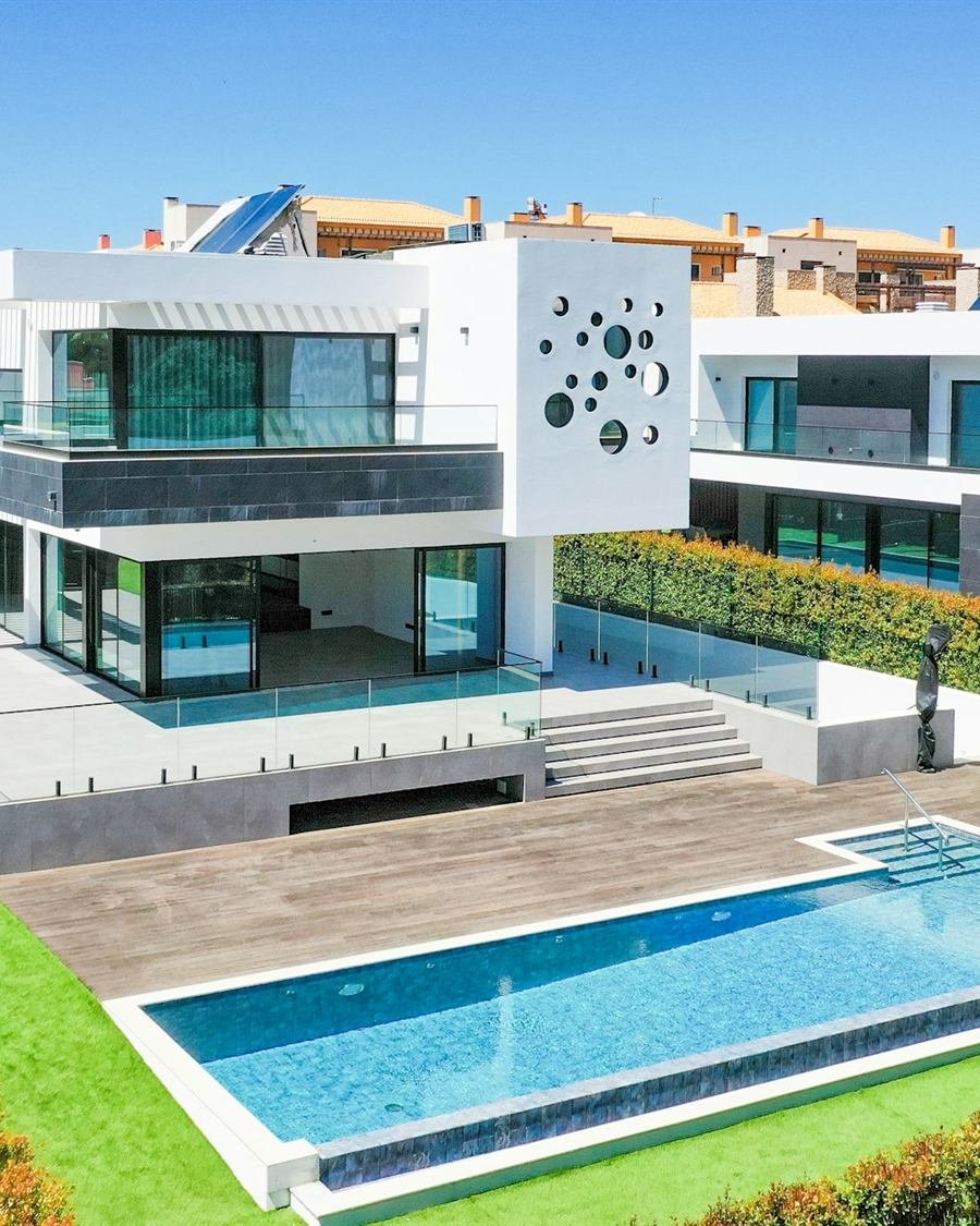 Vista aérea de uma moradia branca com piscina, terraços e jardim relvado