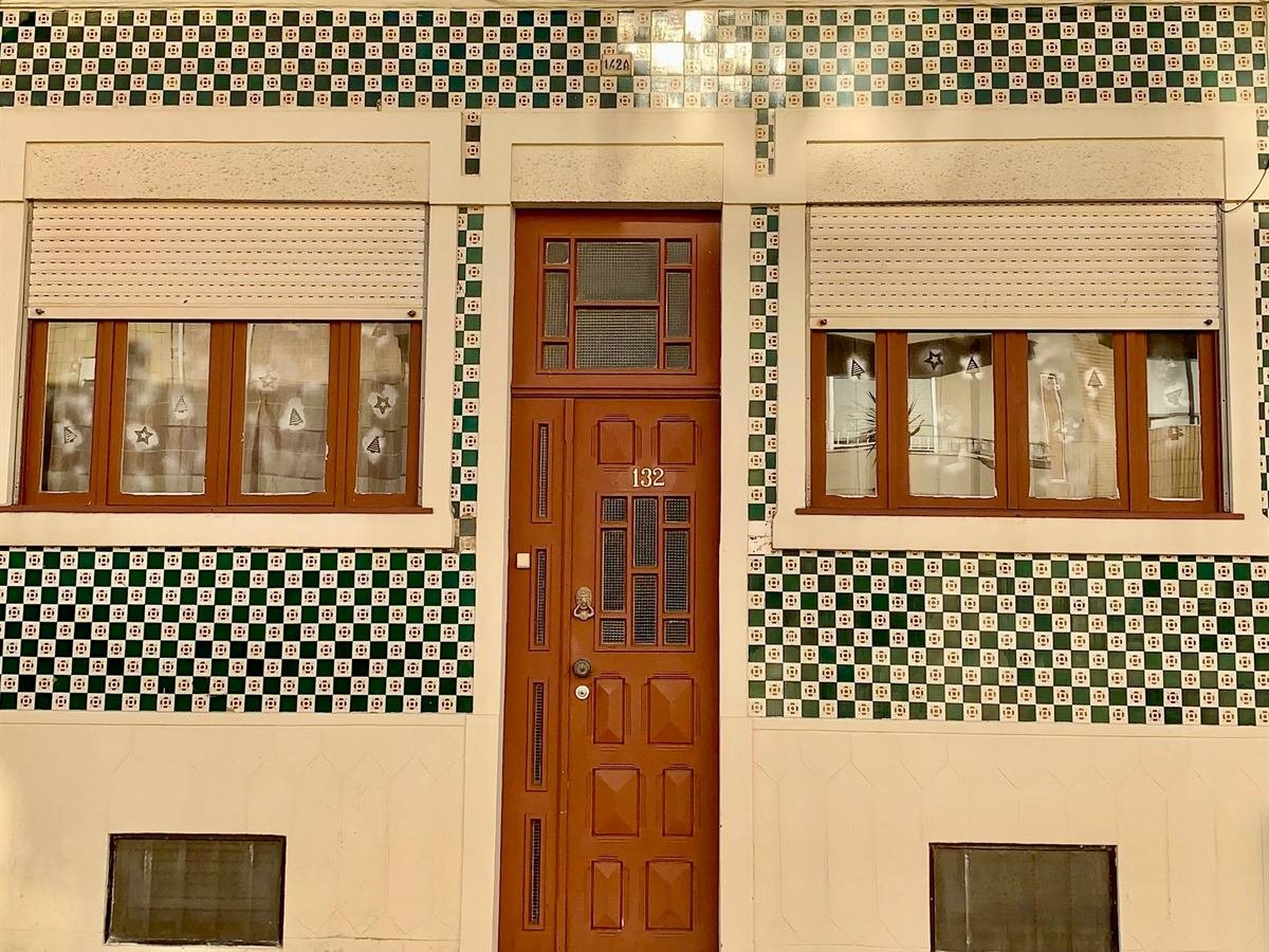 Fachada de casa tradicional revestida a azulejos portugueses verdes, com porta de madeira