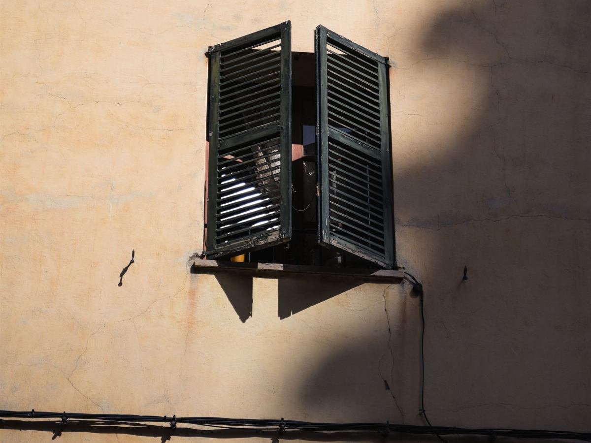 Fachada rústica mediterrânica com portadas verdes de madeira e sombras ao sol